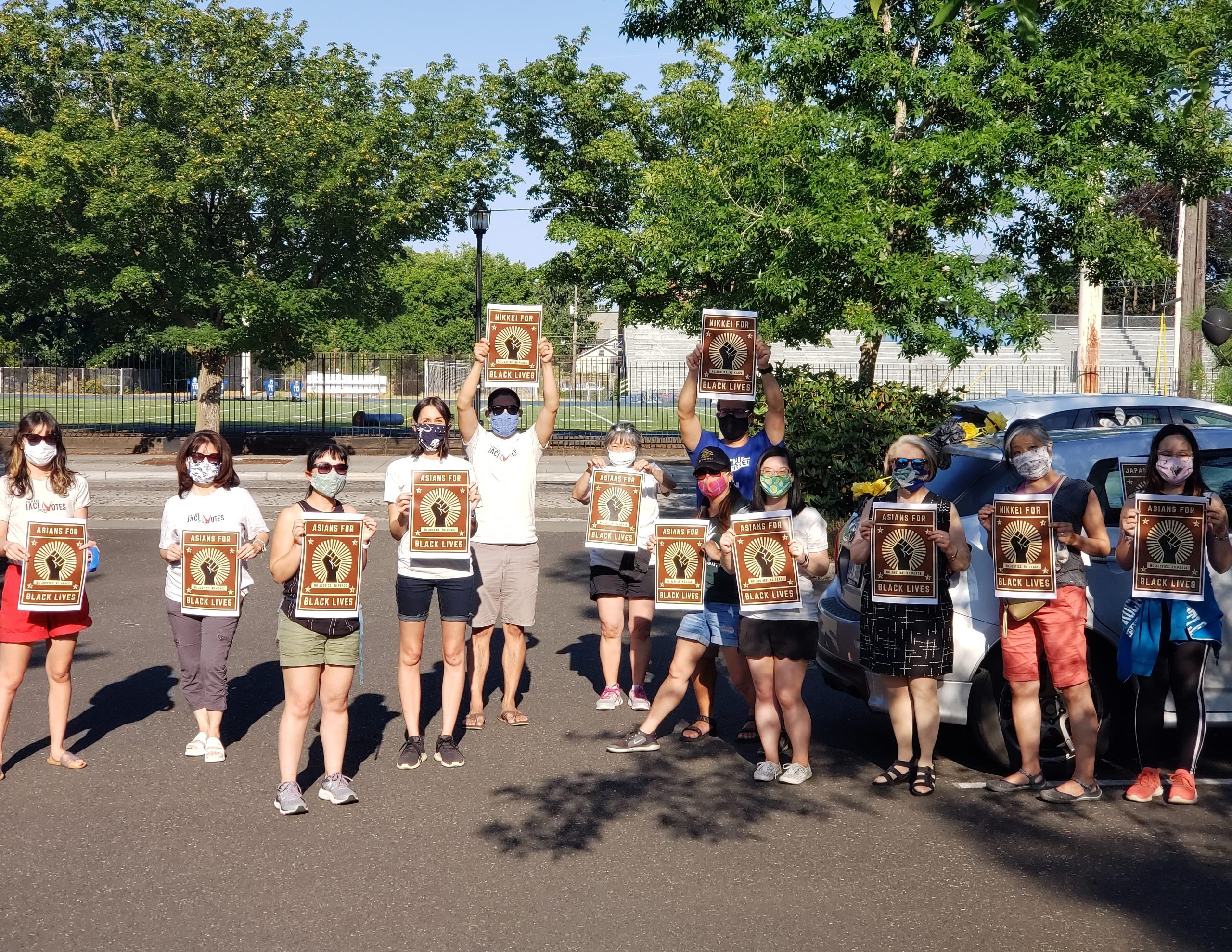 Portland JACL members hold up "Nikkei for Black Lives" signs before a car caravan protest